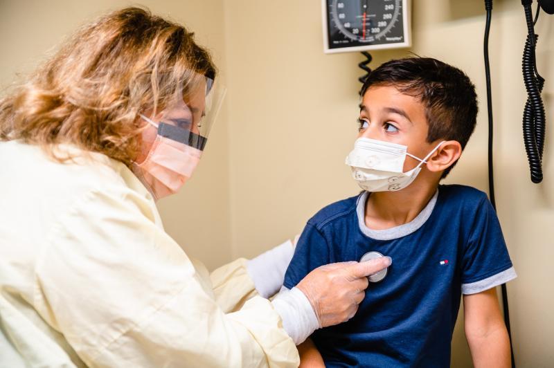 a medical provider listening to the heart of a boy wearing a mask